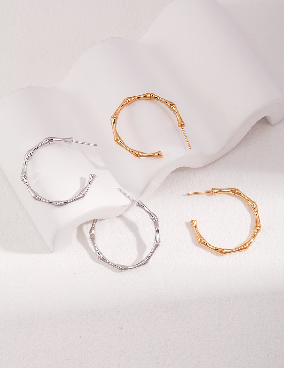 Collection of gold and silver hoop earrings displayed on white surface, with 2 pairs of bamboo half hoop earrings in silver and gold.