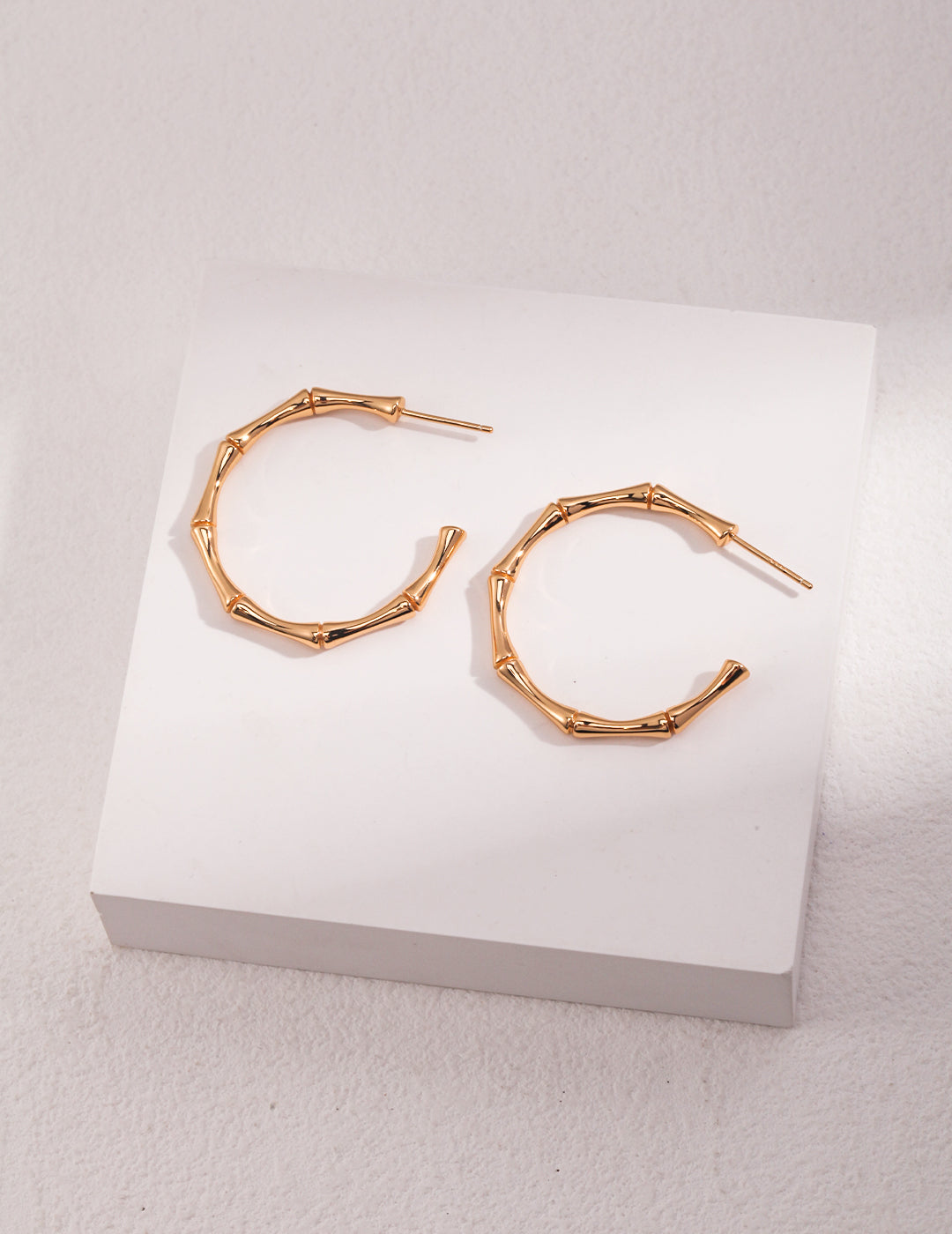 Gold bamboo half hoop earrings on a white surface.