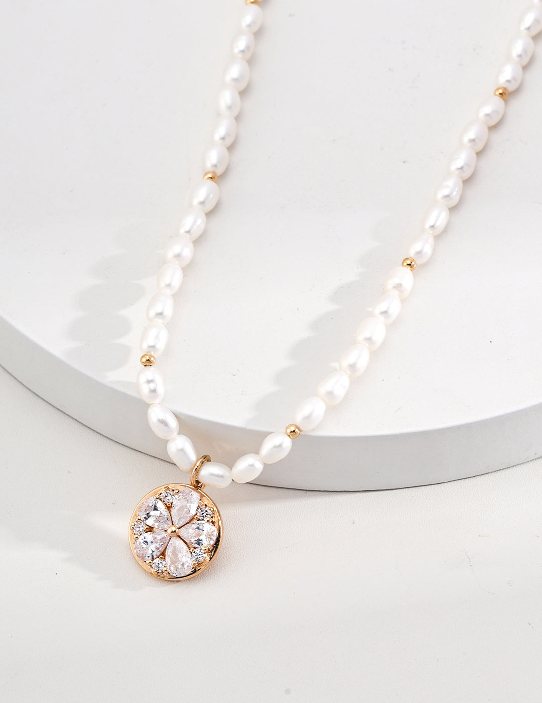 Detailed shot of gold plated pendant on white pearl necklace.