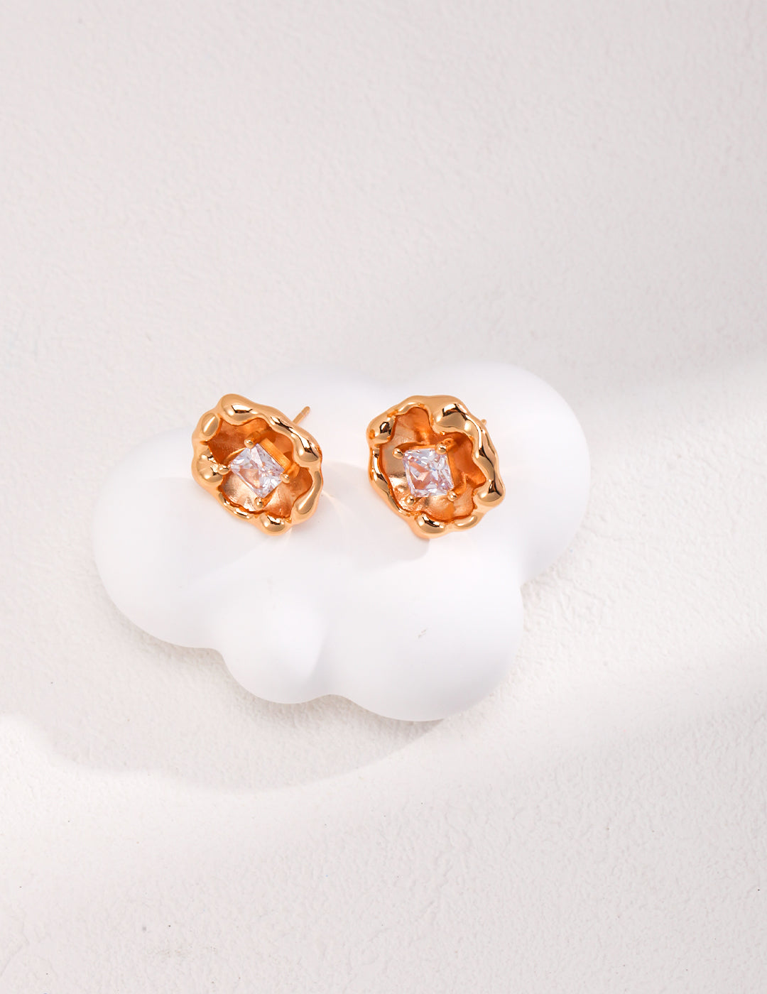 A pair of gold earrings featuring diamond accents and cubic zirconia, elegantly placed on a soft cloud, like blooming flowers.