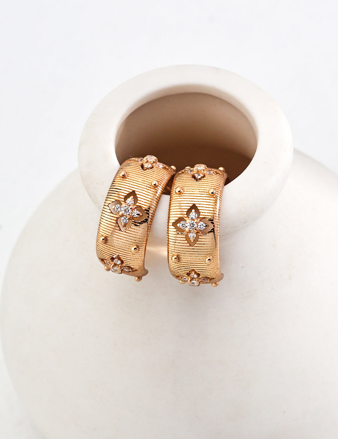 Florence gold hoops by Mezuille displayed over a minimalist white ceramic vase, highlighting their architectural form.