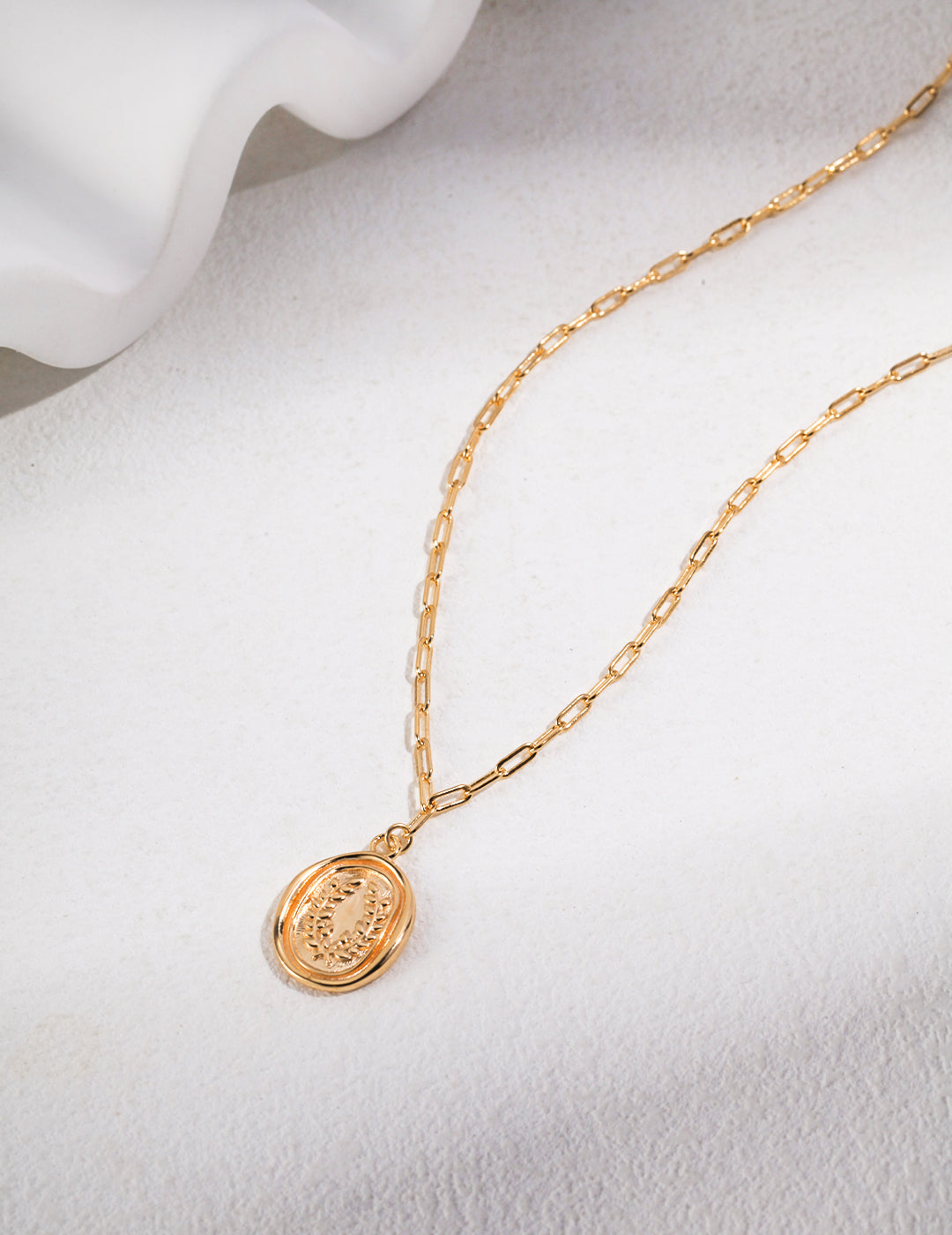 Gold plated coin pendant necklace on white surface.