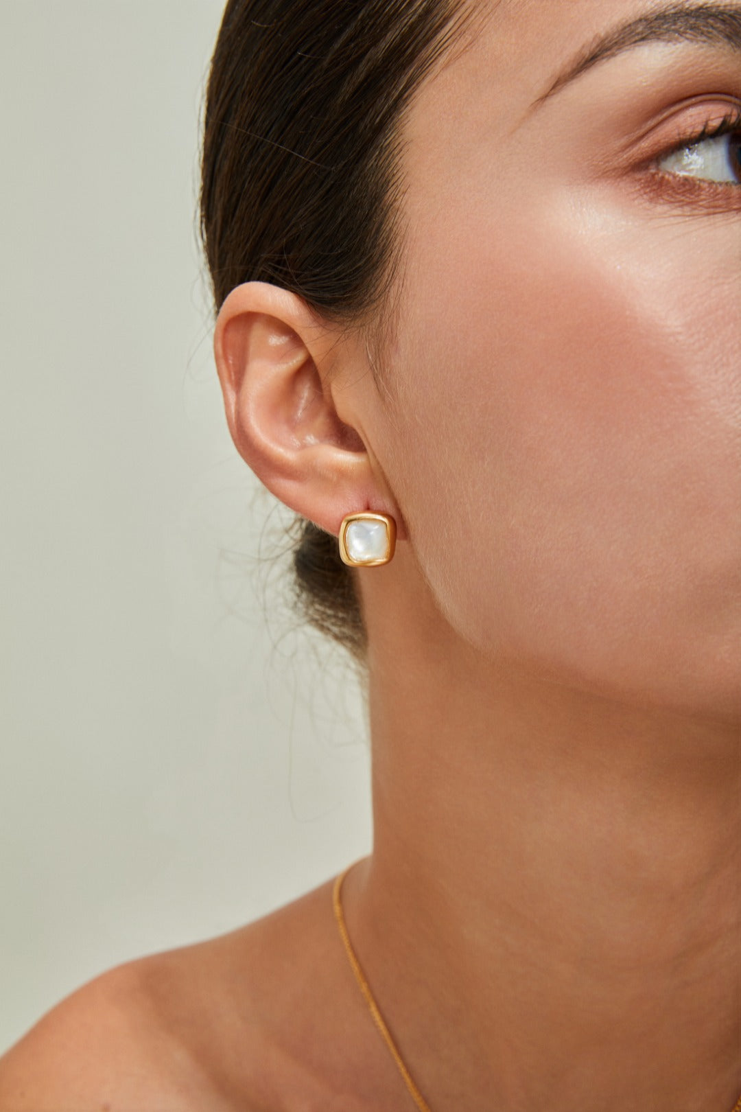 Close-up of a woman wearing a gold earring adorned with a squared nacre, highlighting her sophisticated style.