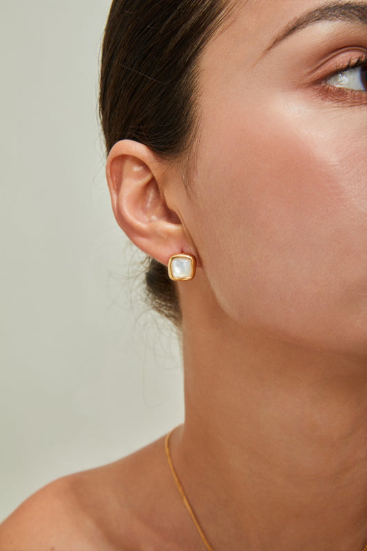 Close-up of a woman wearing a gold earring adorned with a squared nacre, highlighting her sophisticated style.