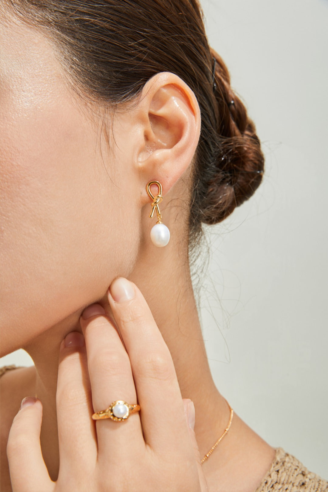 A woman elegantly wears a gold ring and a pearl earring, embodying grace and timeless beauty in her accessories.