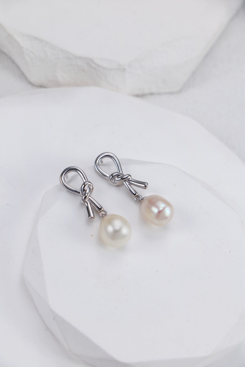 White pearl earrings elegantly placed on a white marble surface, emphasizing their sophistication and charm.