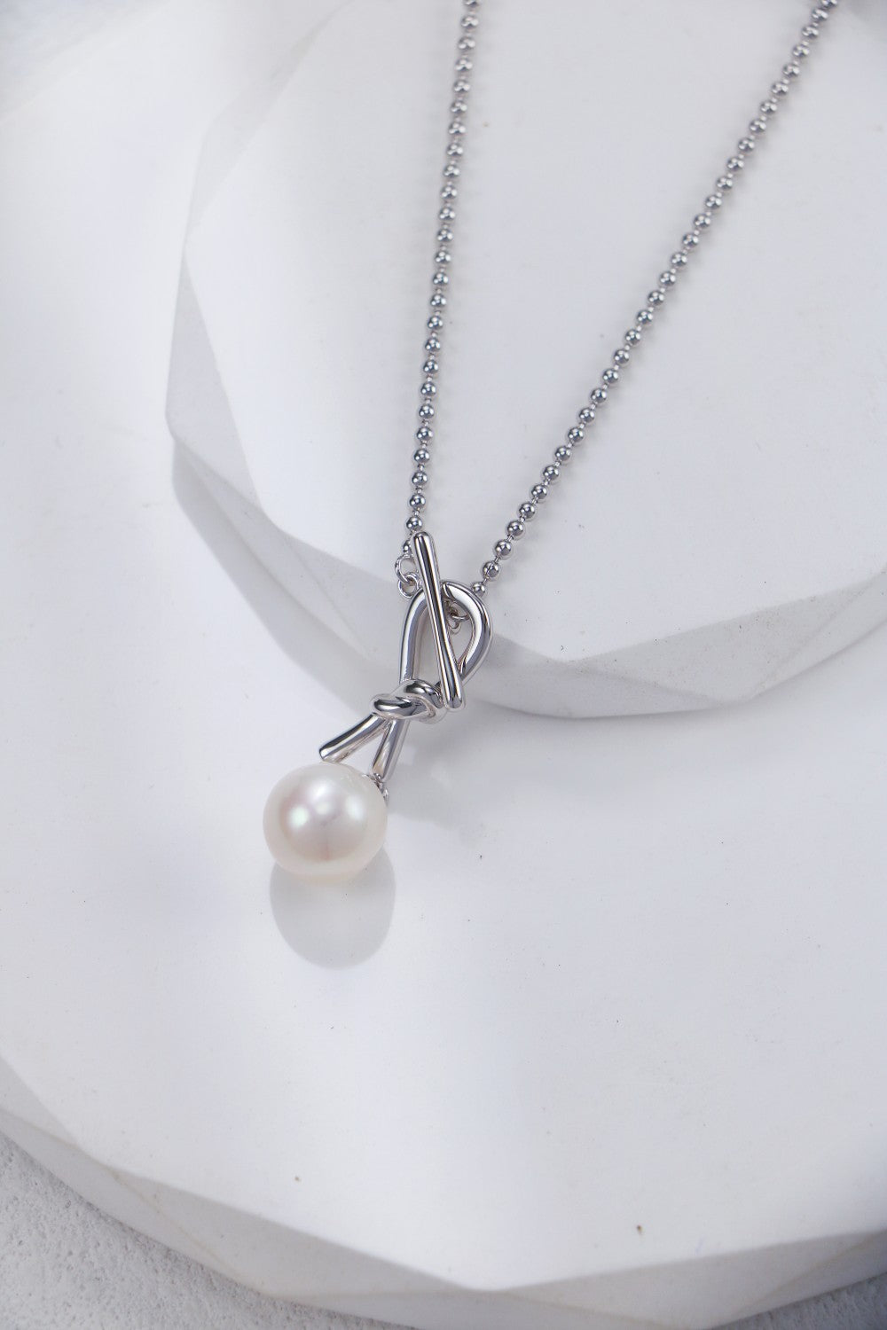 A stunning white pearl necklace with knots, resting gracefully on a white table surface.