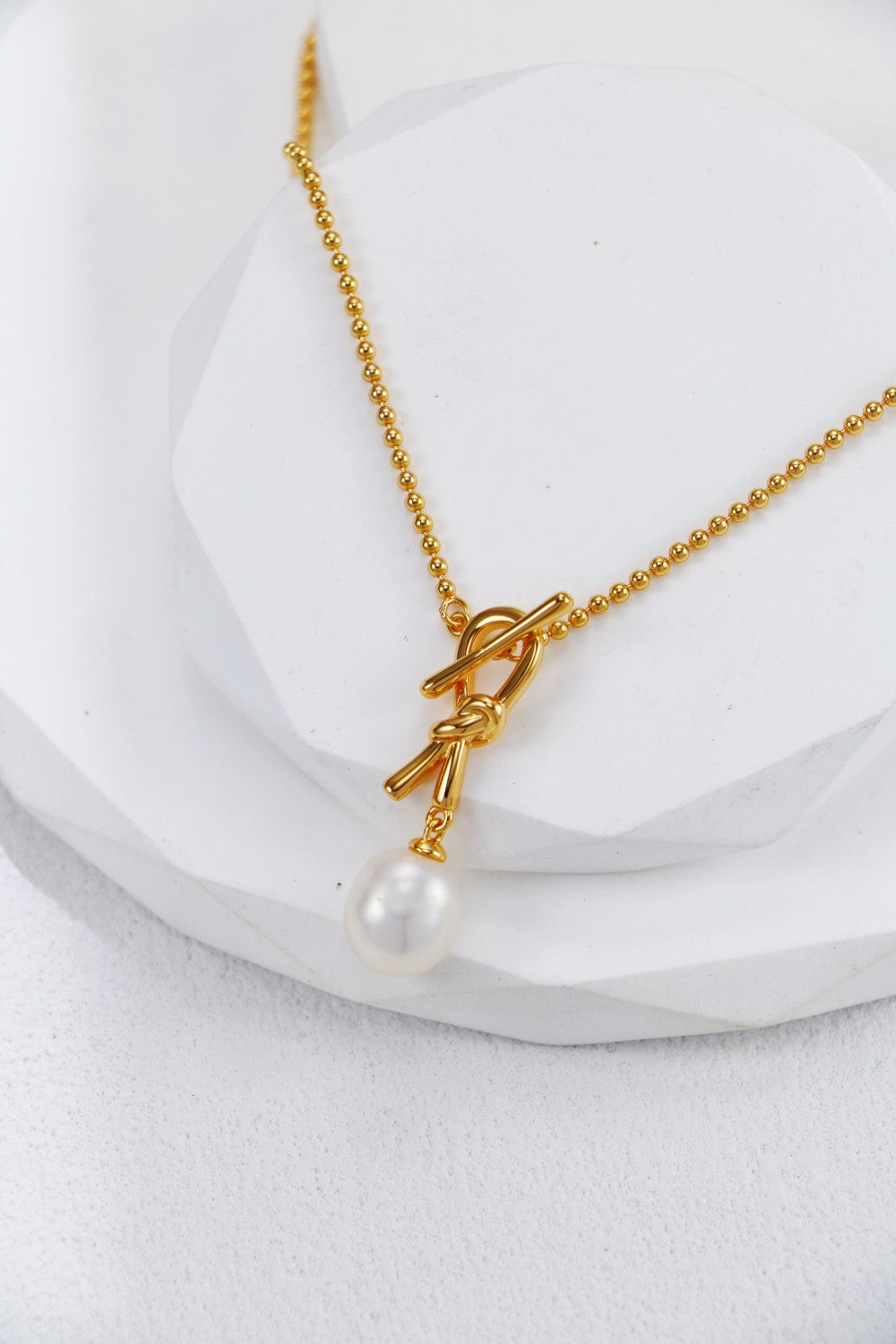 Elegant gold plated necklace with a pearl centerpiece and a stylish knot design, perfect for any occasion.