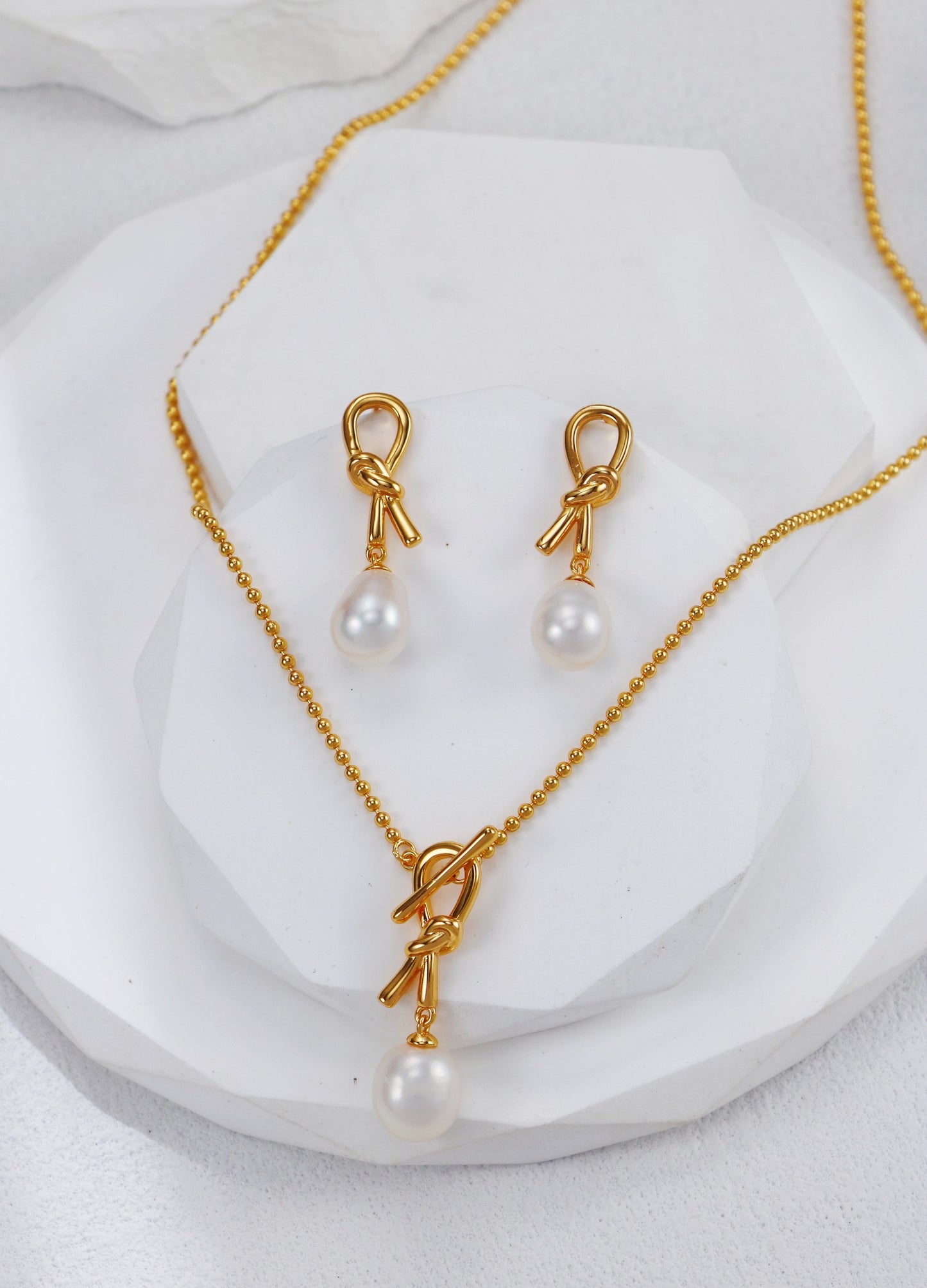 Stunning gold-plated necklace with a knot design and matching pearl earrings, perfect for any elegant occasion.