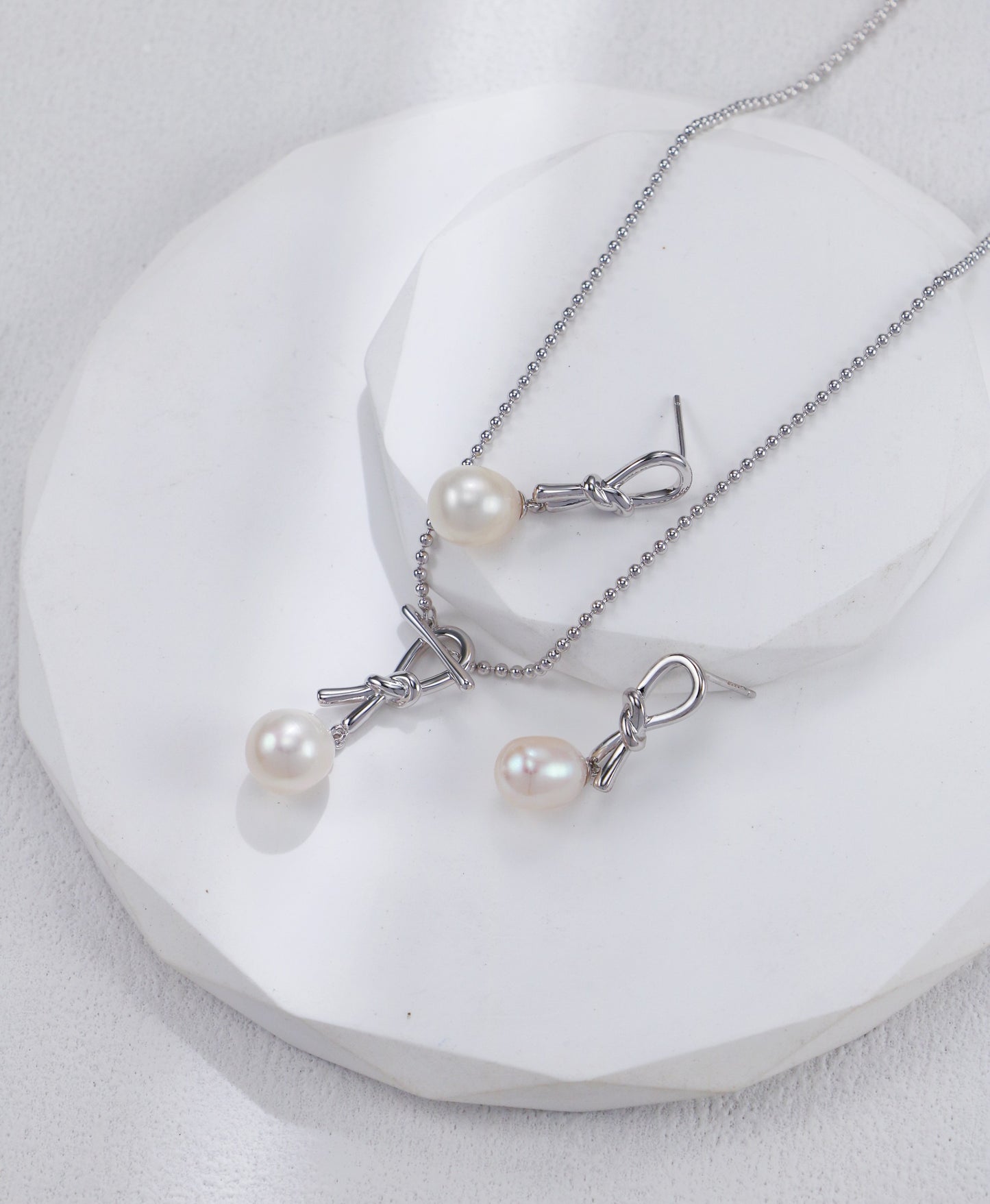  A stunning white pearl knot necklace paired with matching earrings, beautifully arranged on a white plate.