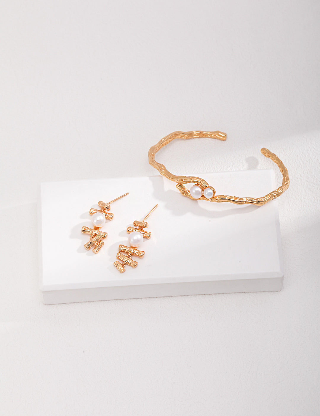 Elegant gold jewelry set on a white surface, including a gold torque bangle with freshwater pearls and complementing earrings.