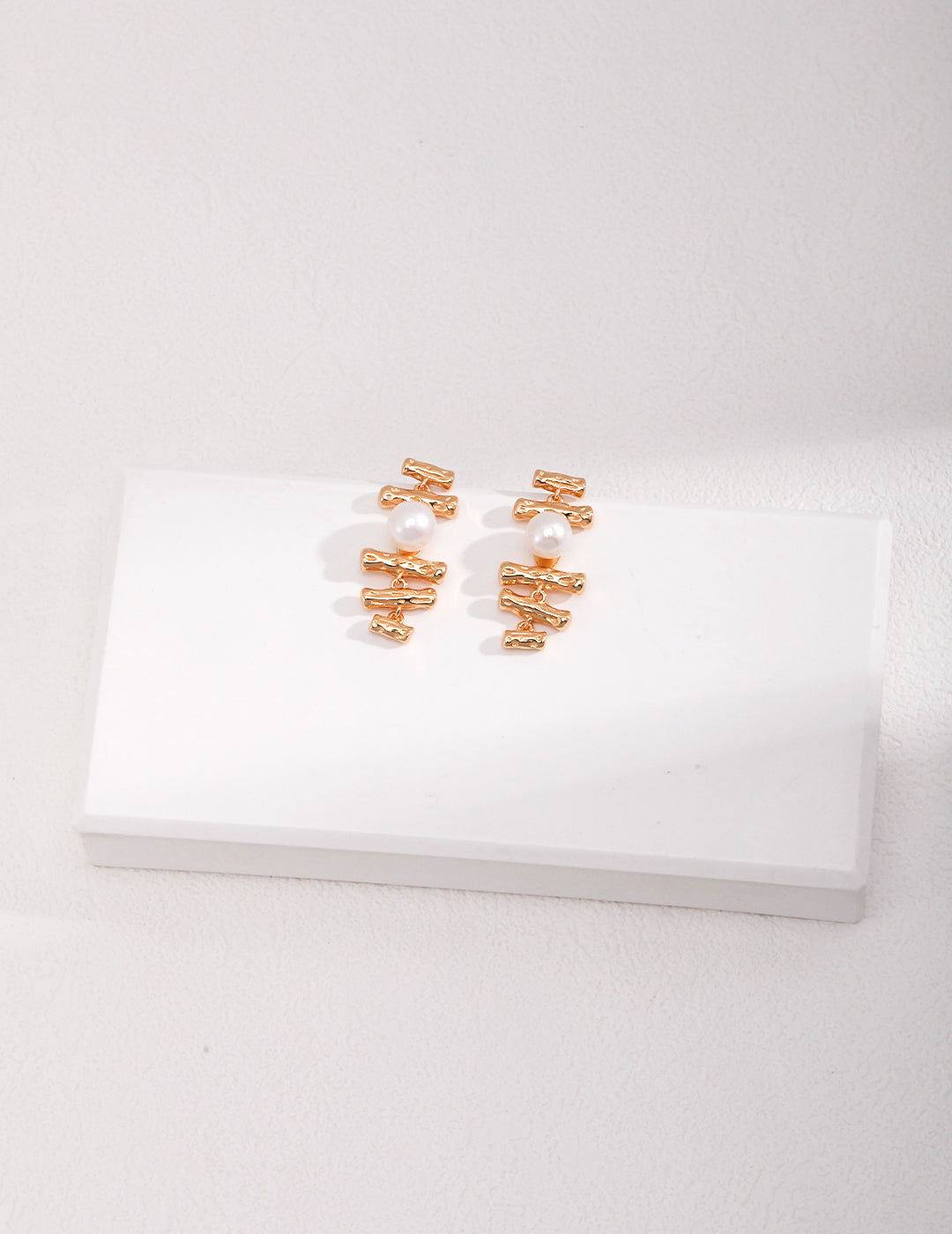 Gold plated earrings with freshwater pearls on a white surface.