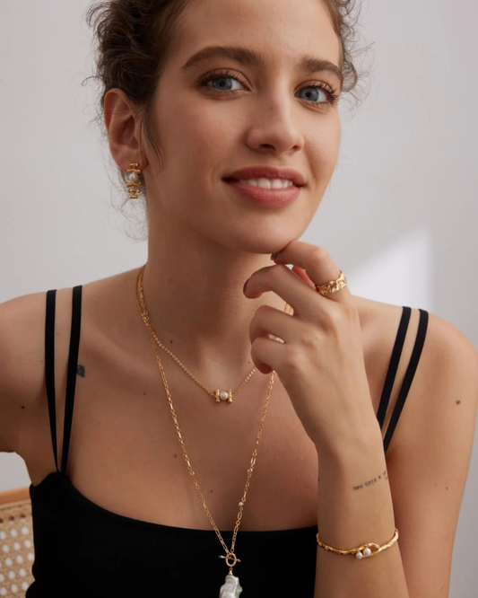 A woman elegantly wears a matching gold necklace and earrings, exuding sophistication and style.