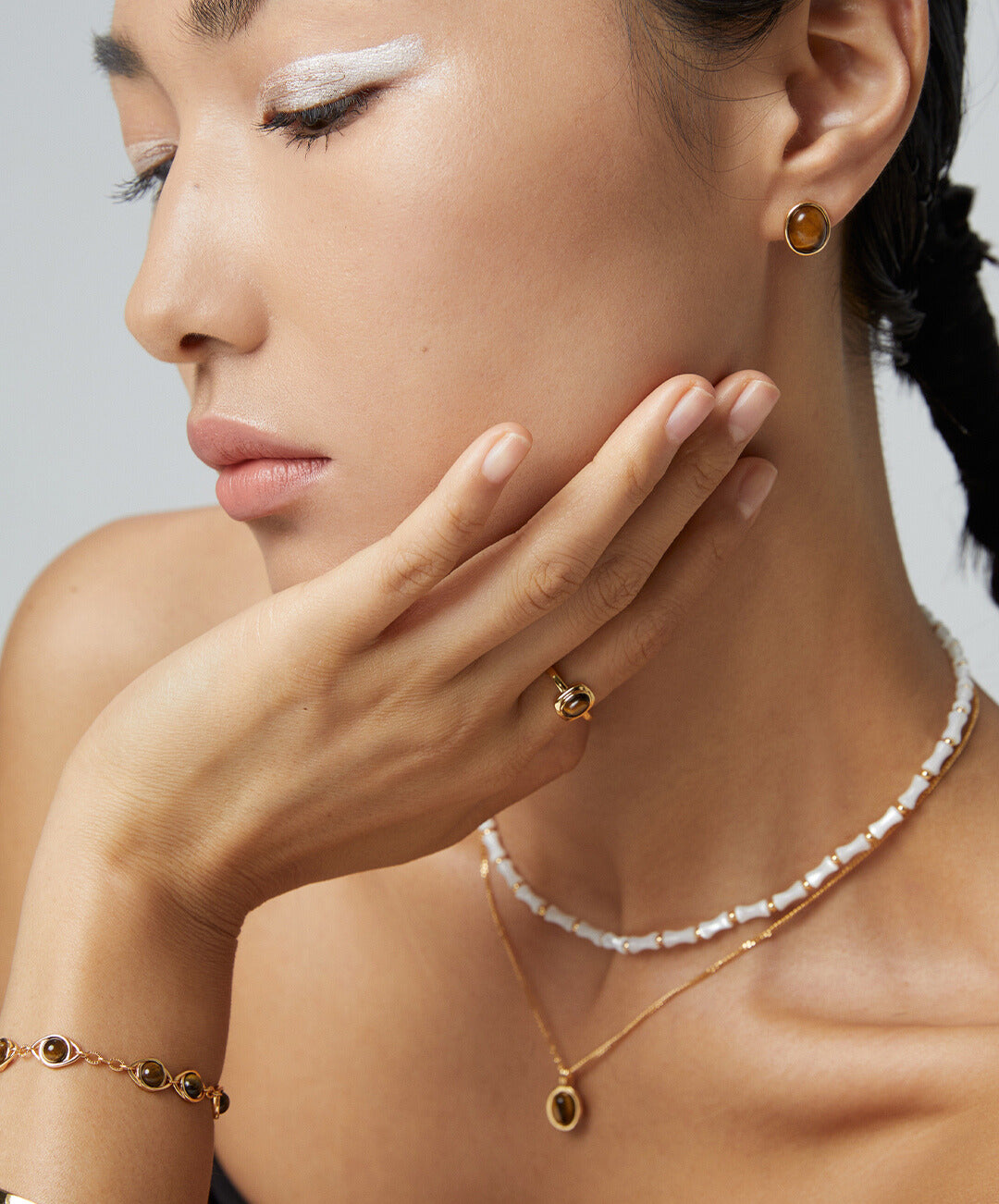 A stylish woman wearing a necklace and earrings, complemented by a gold ring with tiger's eye and matching jewelry.