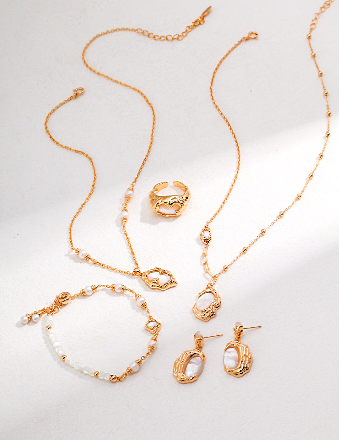 A luxurious set of gold jewelry, including a necklace, bracelet, and earrings. The gold plated bracelet is adorned with nacre, silk shells, and freshwater pearls, complementing the other matching pieces.