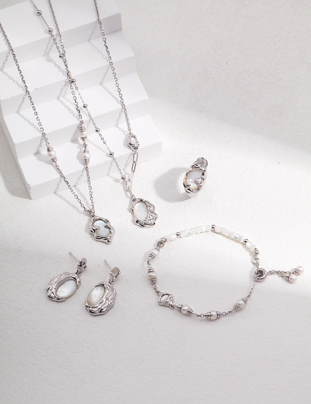 A stunning collection of jewelry on a white surface, featuring a silver bracelet with nacre, silk shells, freshwater pearls, and more.