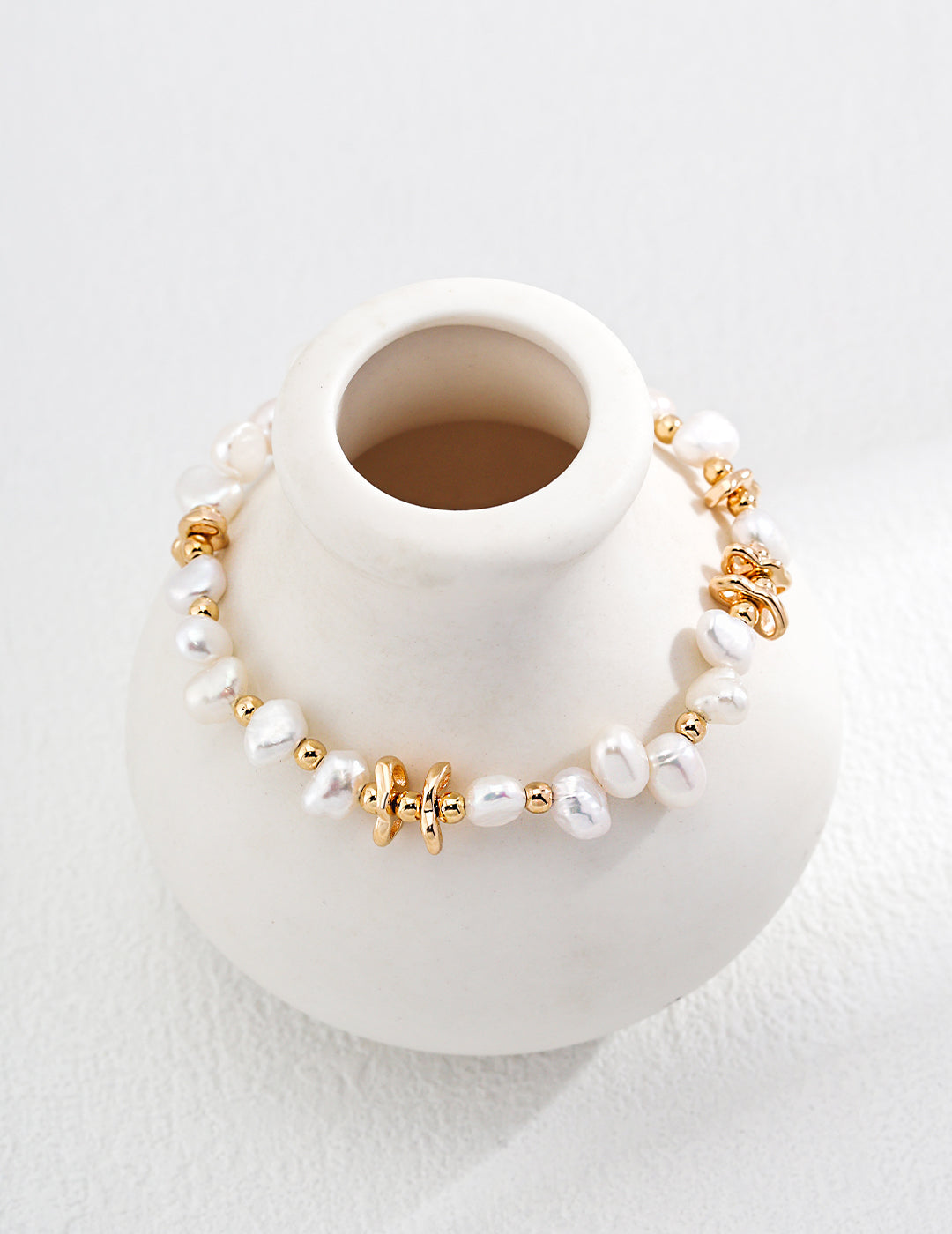 A white vase with a gold and white bracelet, featuring a luxurious gold plated freshwater pearls bracelet.