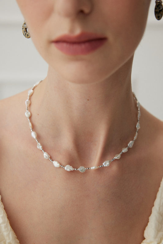 Close-up of a woman wearing an elegant necklace made with delicate baroque pearls, showcasing its luxurious and sophisticated design.