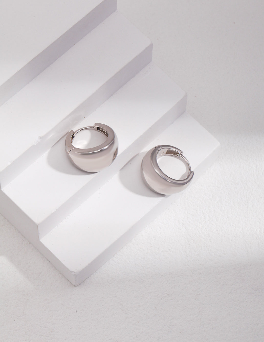 A pair of silver chubby hoops on white background.