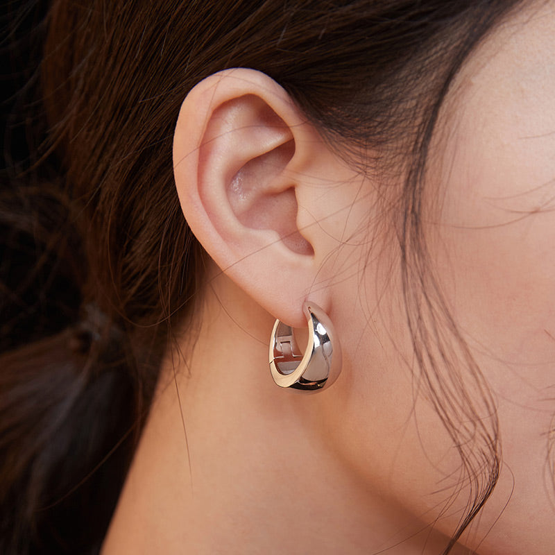 A model wearing silver chubby hoop earrings with an intricate design.