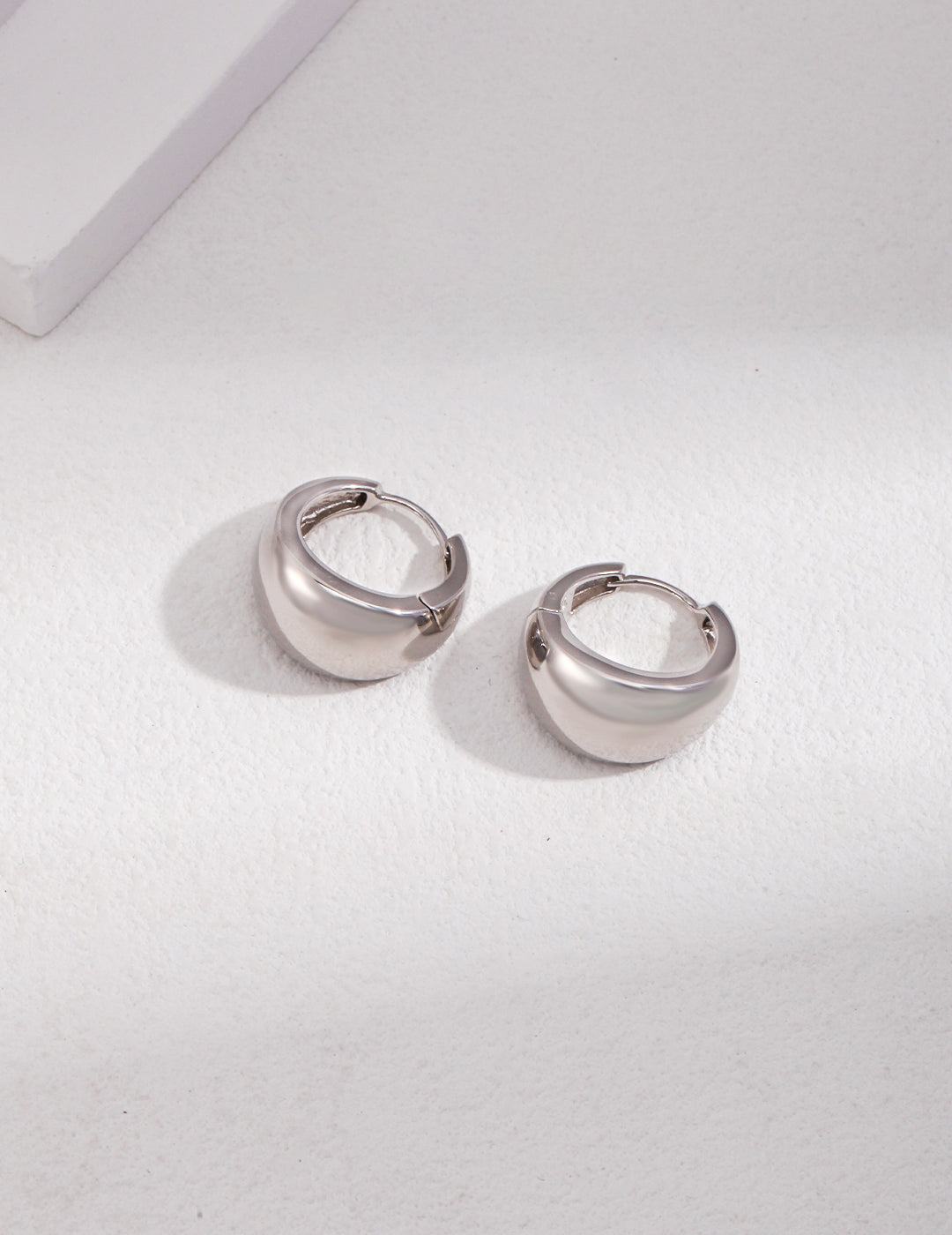 A pair of silver chubby hoop earrings on a white surface.