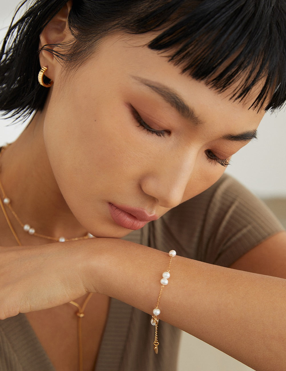 Close up of model wearing a pearl bracelet and gold jewelry from Mezuille.