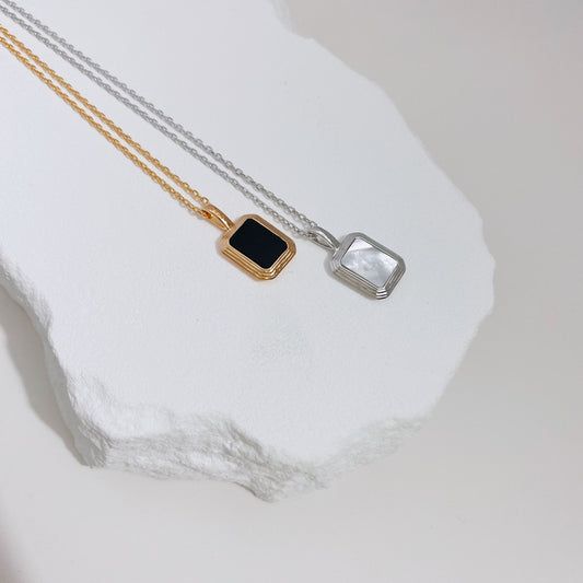 Two gold and silver necklaces featuring a two-way pendant with black agate and shell pearl, displayed on a white surface.