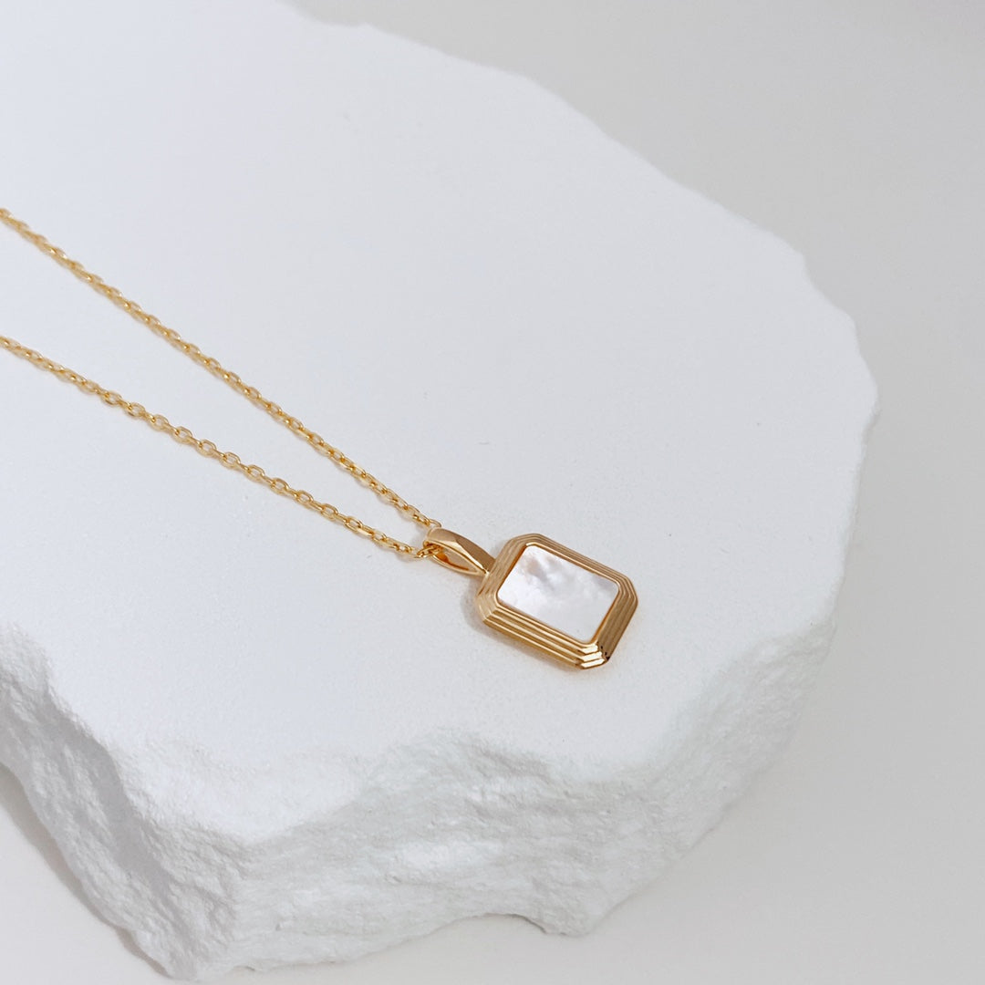 Gold necklace featuring a square  reversible pendant with black agate on one side and shell pearl on the other.