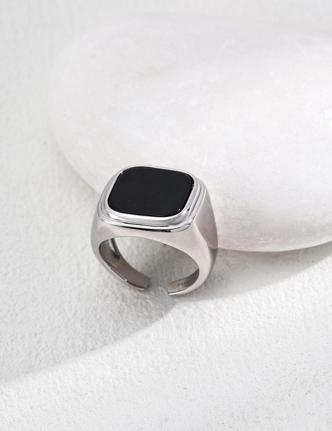 A black stone ring made of agate sits gracefully on a white rock, emphasizing the contrast between dark and light elements.