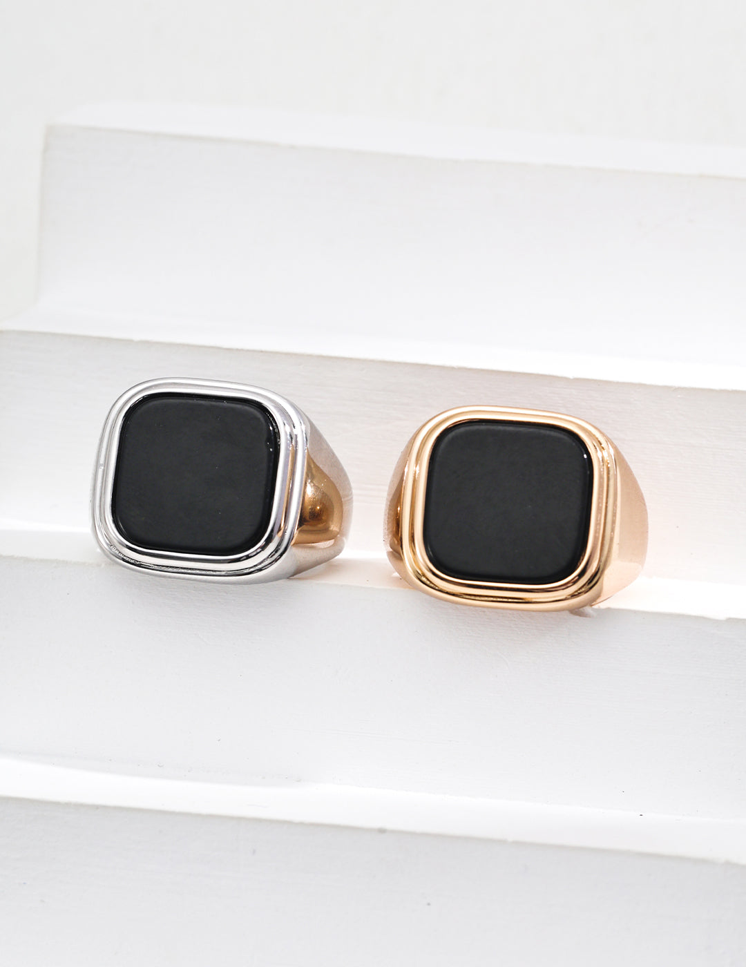 Two stylish black agate rings with gold accents placed on a smooth white surface, highlighting their sophisticated look.