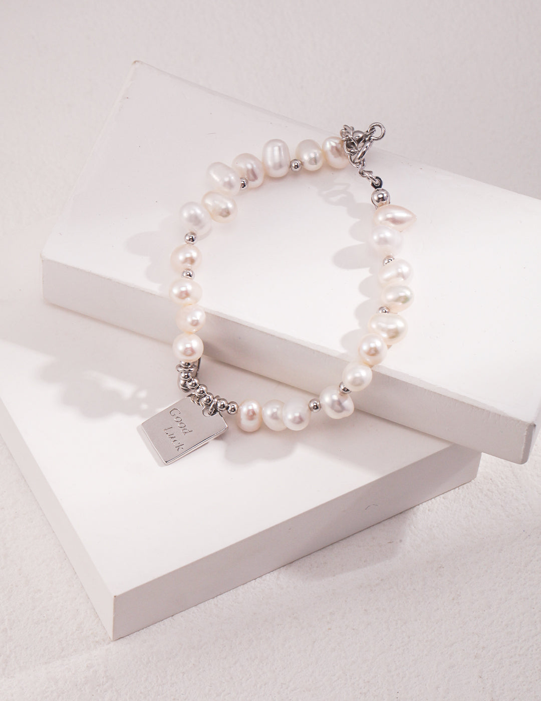 A white pearl bracelet with a silver charm, perfect for adding elegance and sophistication to any outfit.