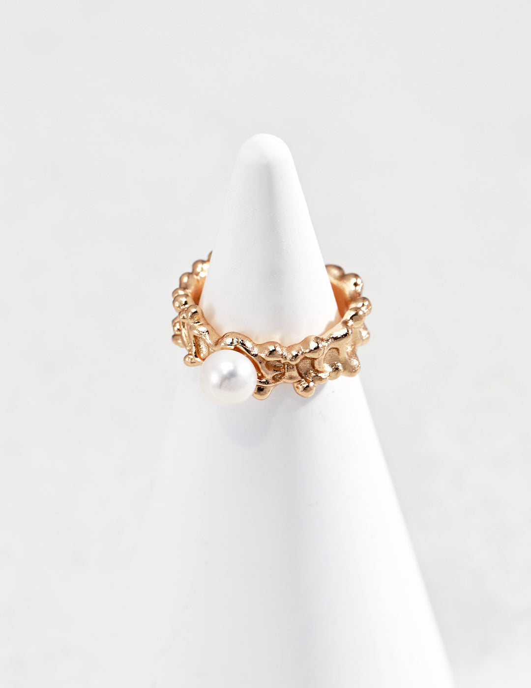 Studio product photograph of the Harper gold ring displayed on a white conical stand. The ring features an organic, textured molten gold band set with a single white freshwater pearl.