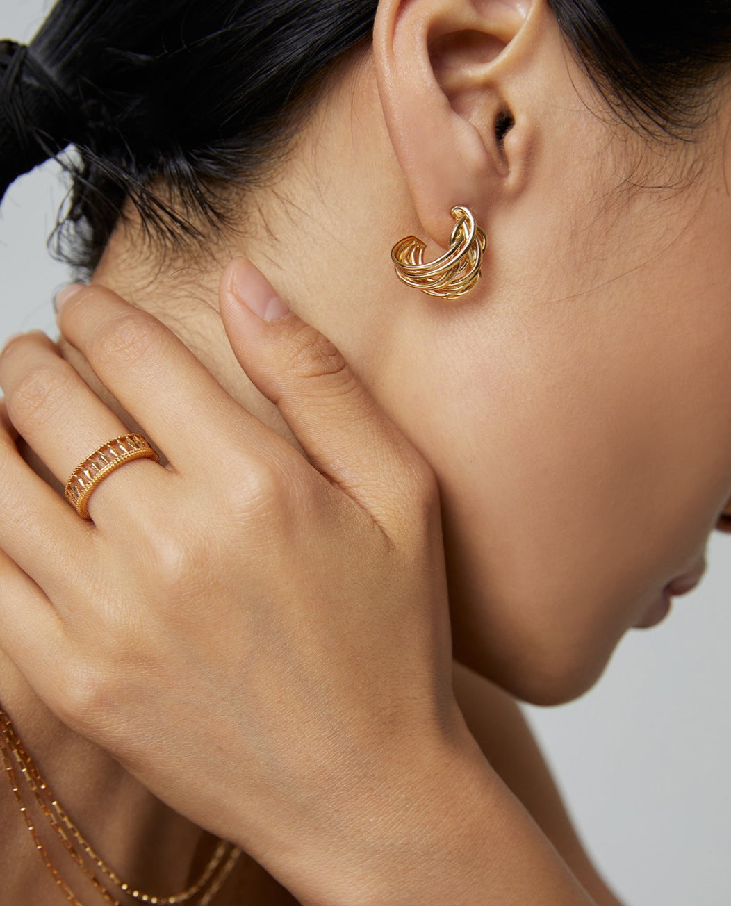 Close up shot of model showcasing her gold jewelry collection, featuring a gold ring