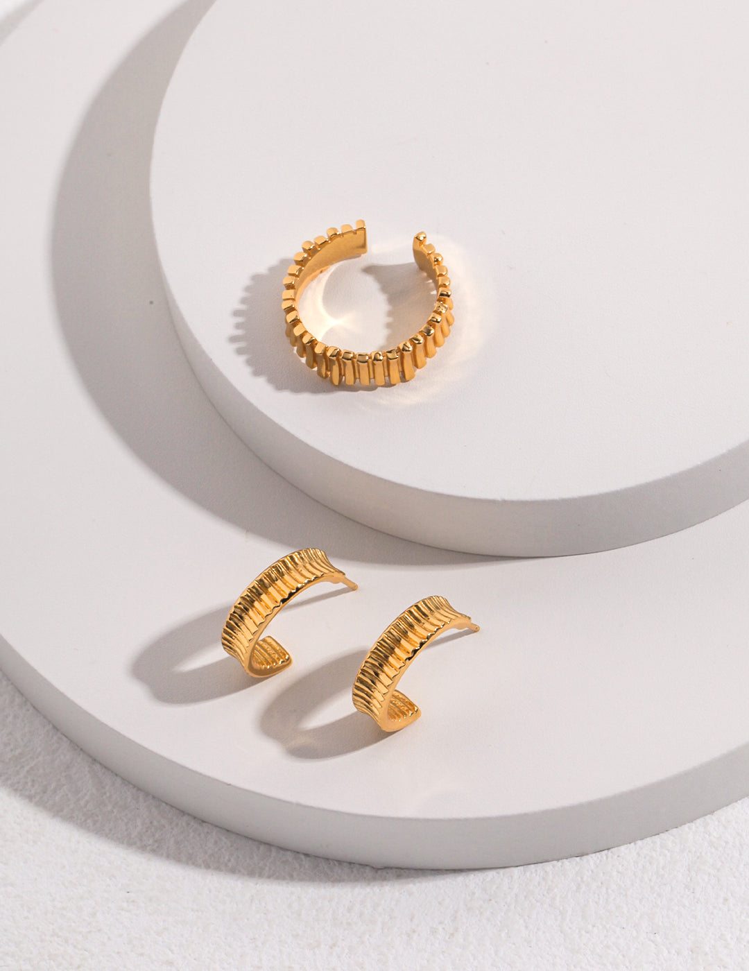 Two gold earrings and a gold ring with fine lines, placed on a white plate.