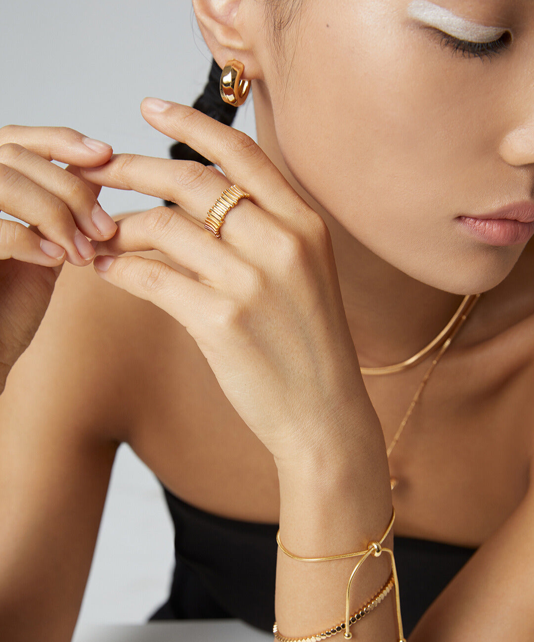 Model showcasing gold jewelry, including a delicate gold ring, in a black top.