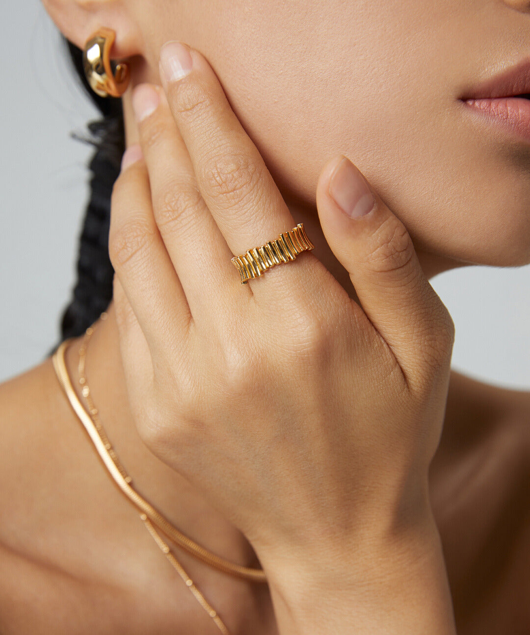 A model showcasing a fine line of gold jewelry, wearing a stunning gold ring and matching earrings.