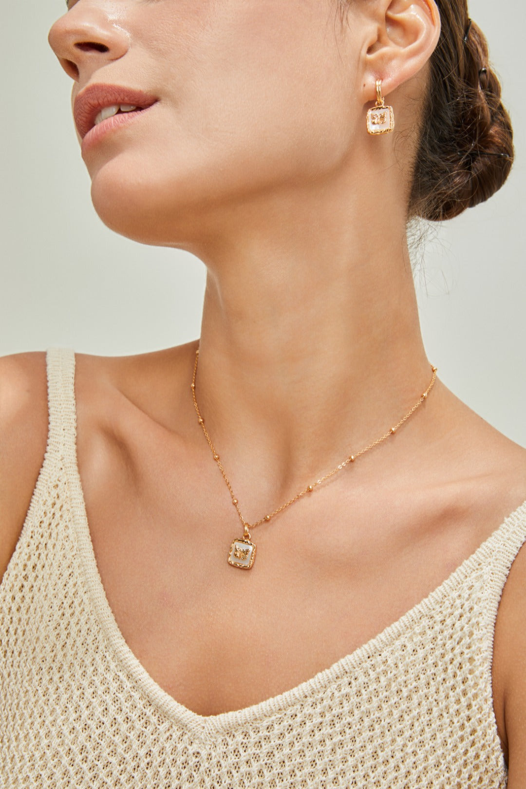 Model in a white tank top adorned with a gold necklace and matching earrings, radiating confidence and fashion.