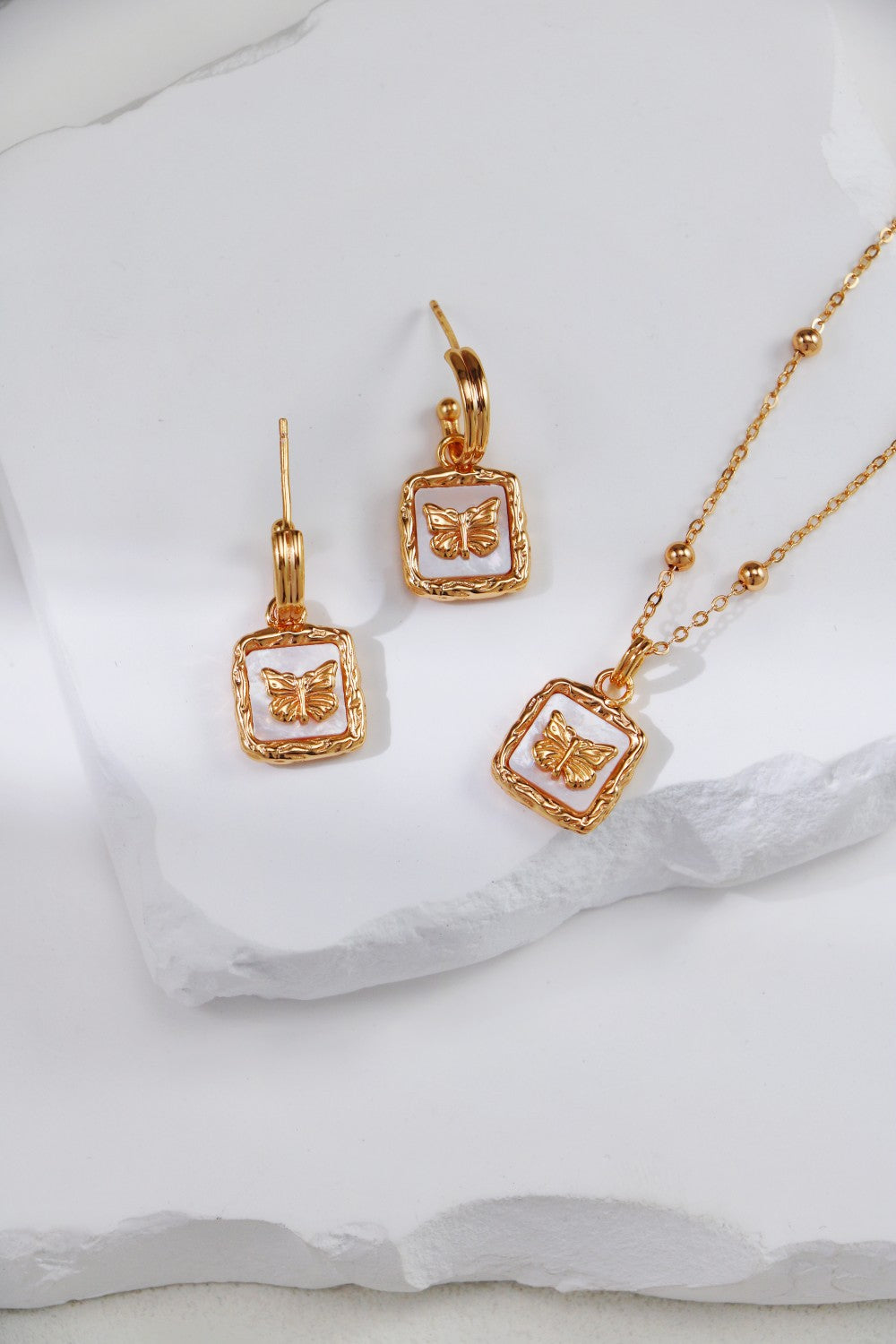 Stunning gold jewelry set with a nacre butterfly stone, including a matching necklace and earrings for a chic look.