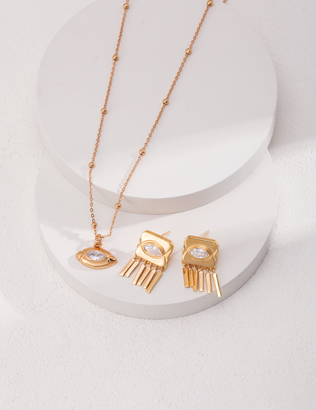 Gold plated necklace and earrings with cubic zirconia olive shape pendant, on white surface.