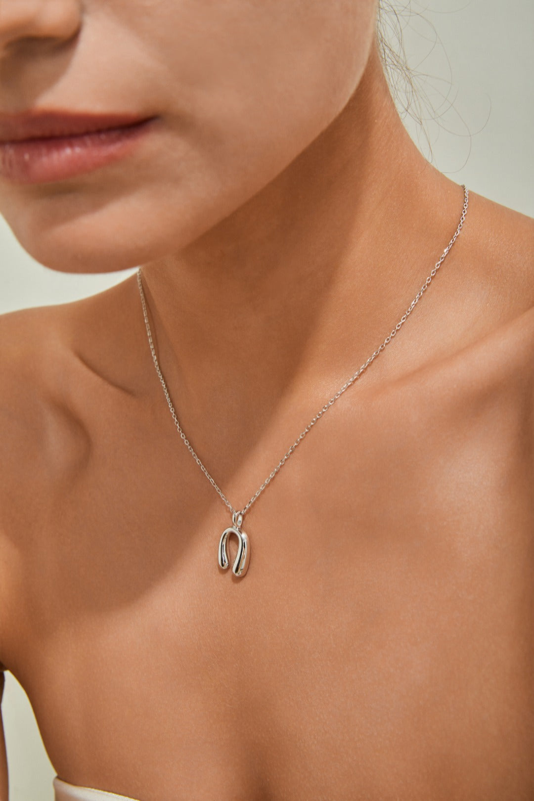 A woman elegantly wears a silver necklace featuring a distinctive horseshoe pendant, symbolizing love and good luck.