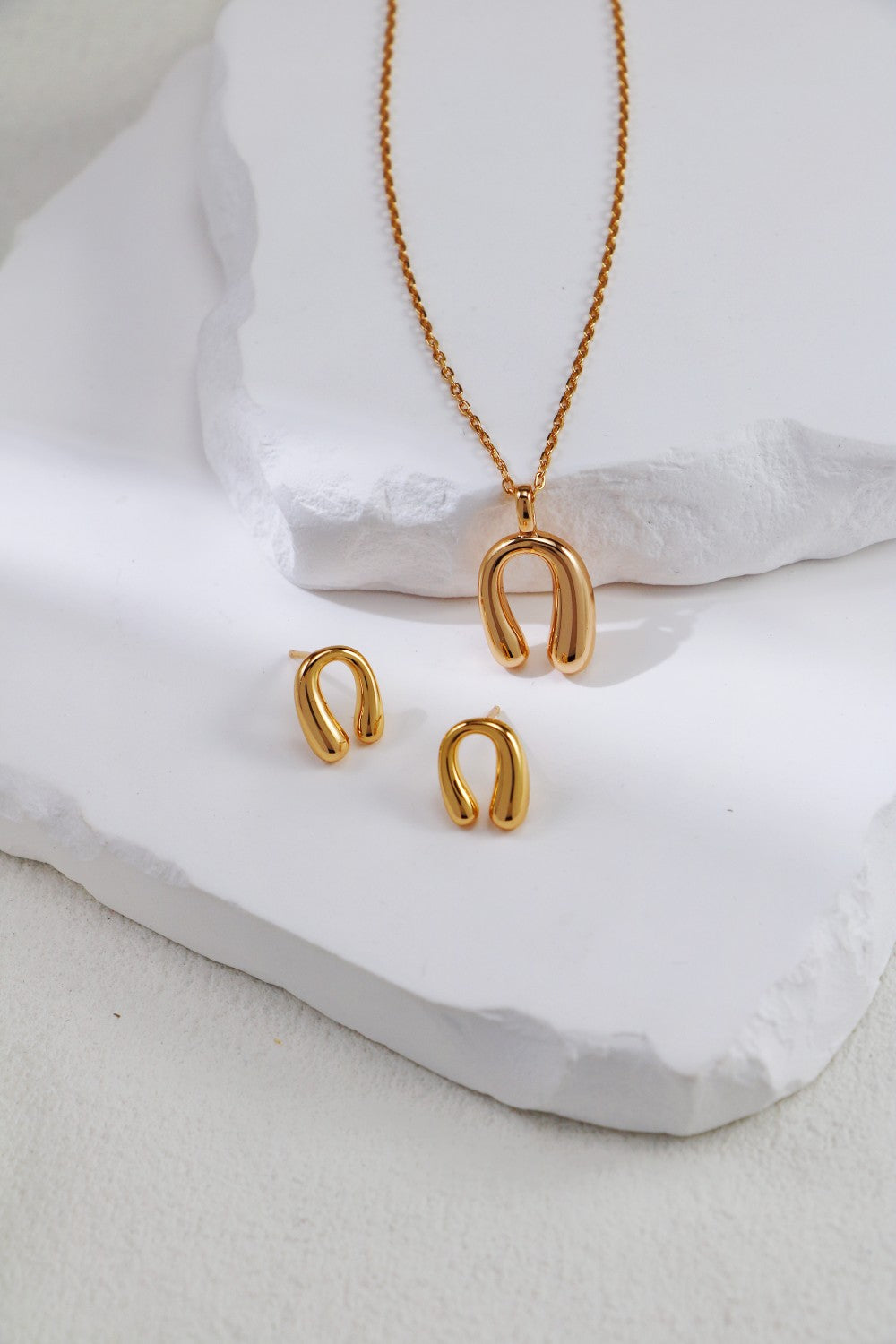 A matching set of gold horseshoe necklace and earrings resting on a pristine white background.