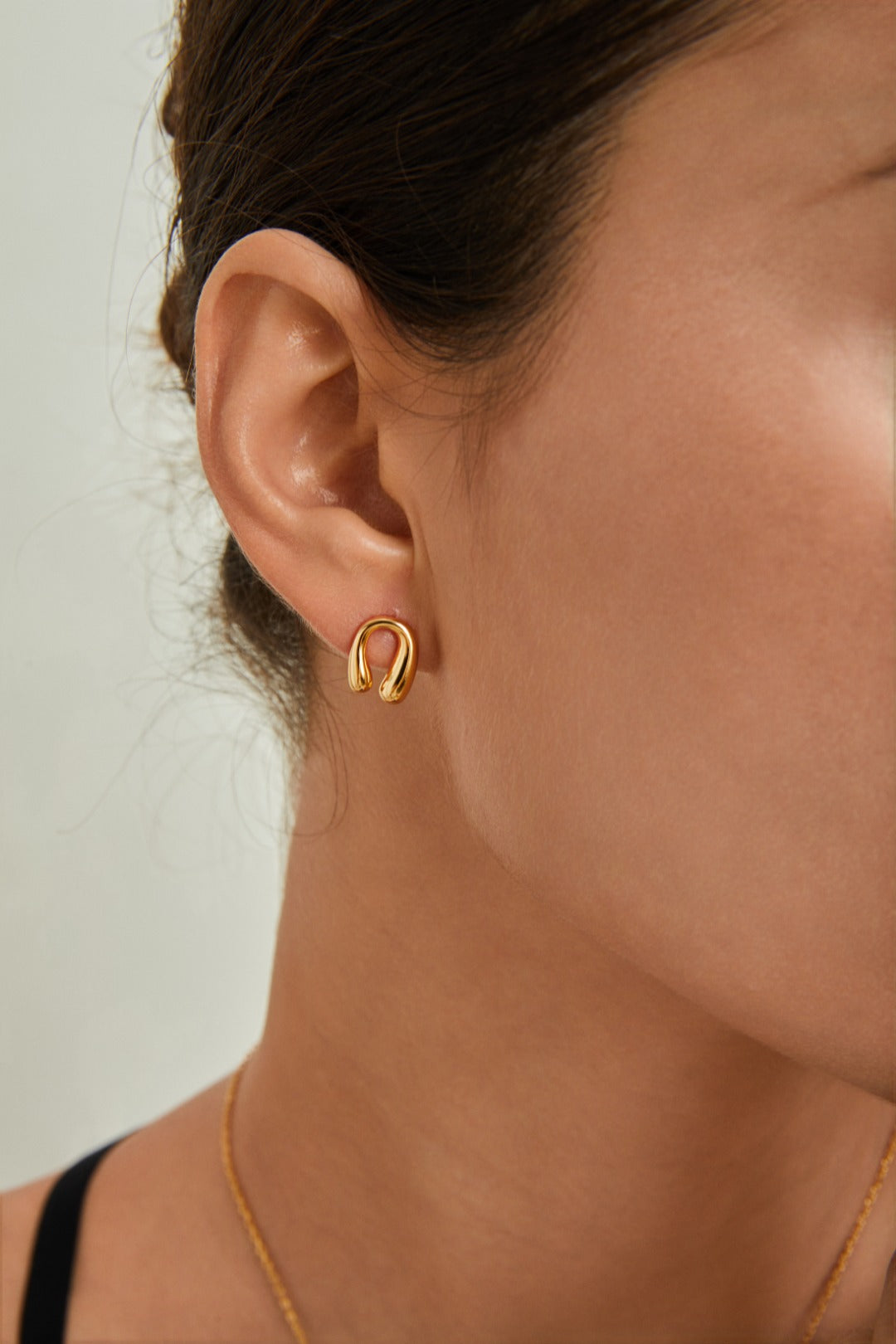 A woman showcases a stylish gold hoop earring, resembling a horseshoe, adding elegance to her look.