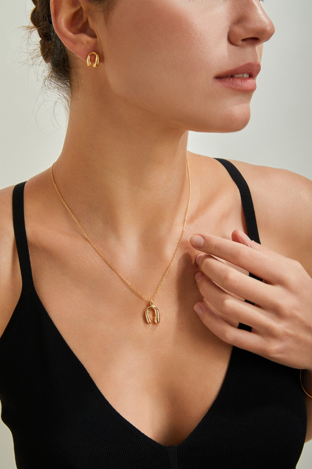 A woman showcases a horseshoe-themed gold necklace and matching earrings, radiating elegance and style.