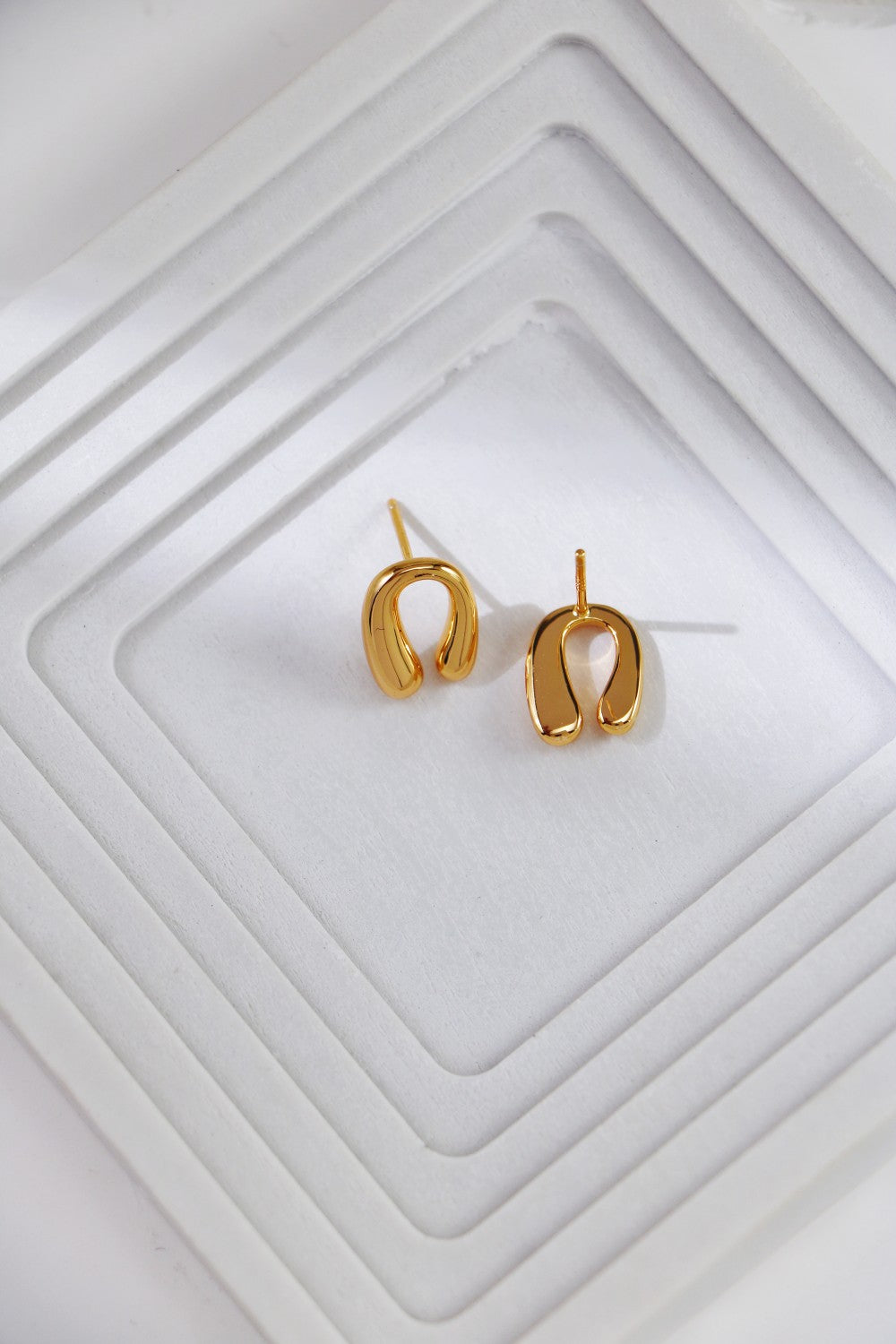 Gold horseshoe earrings resting on a white tray, highlighting their elegant front and back design.