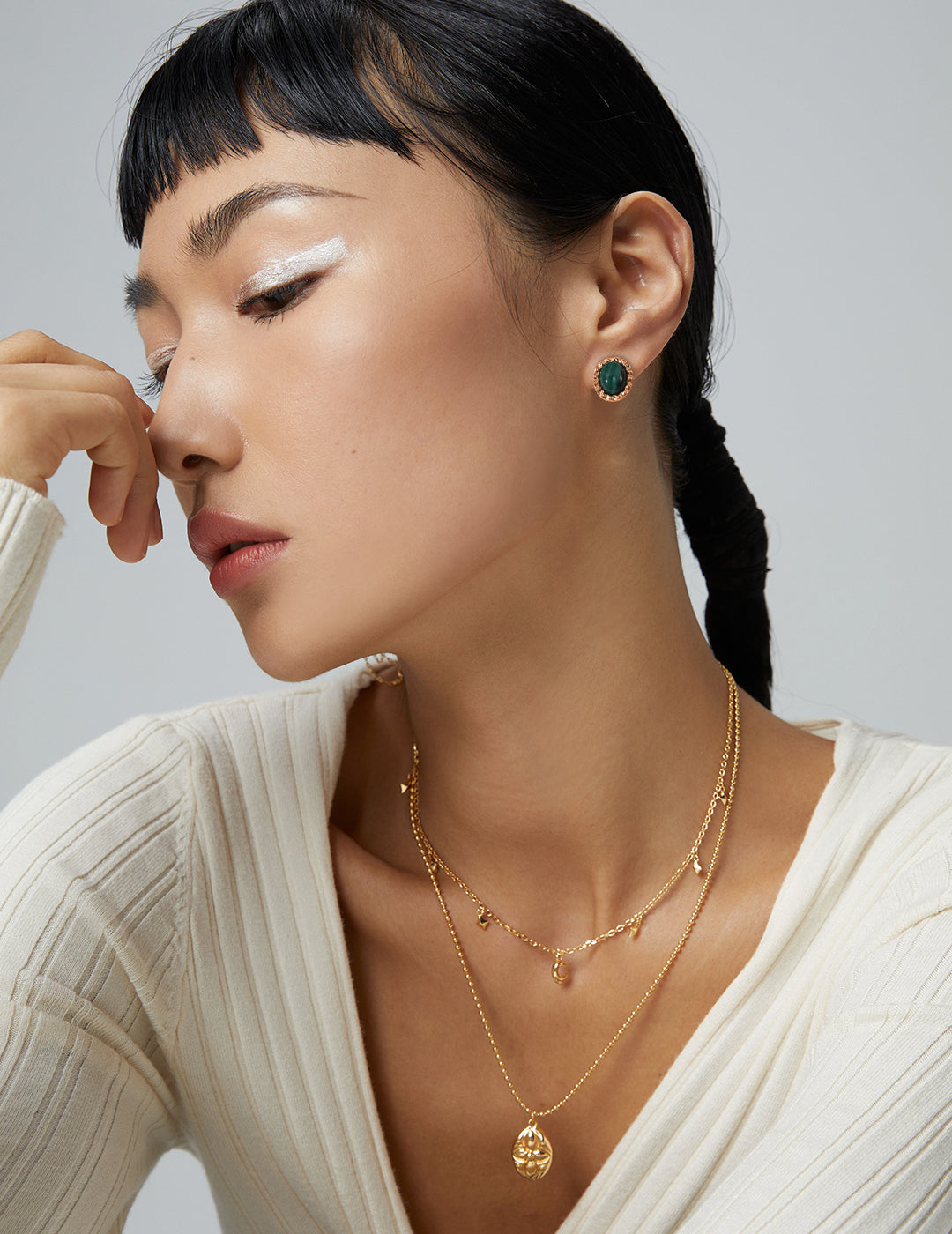 Woman in white sweater accessorized with gold malachite earrings.