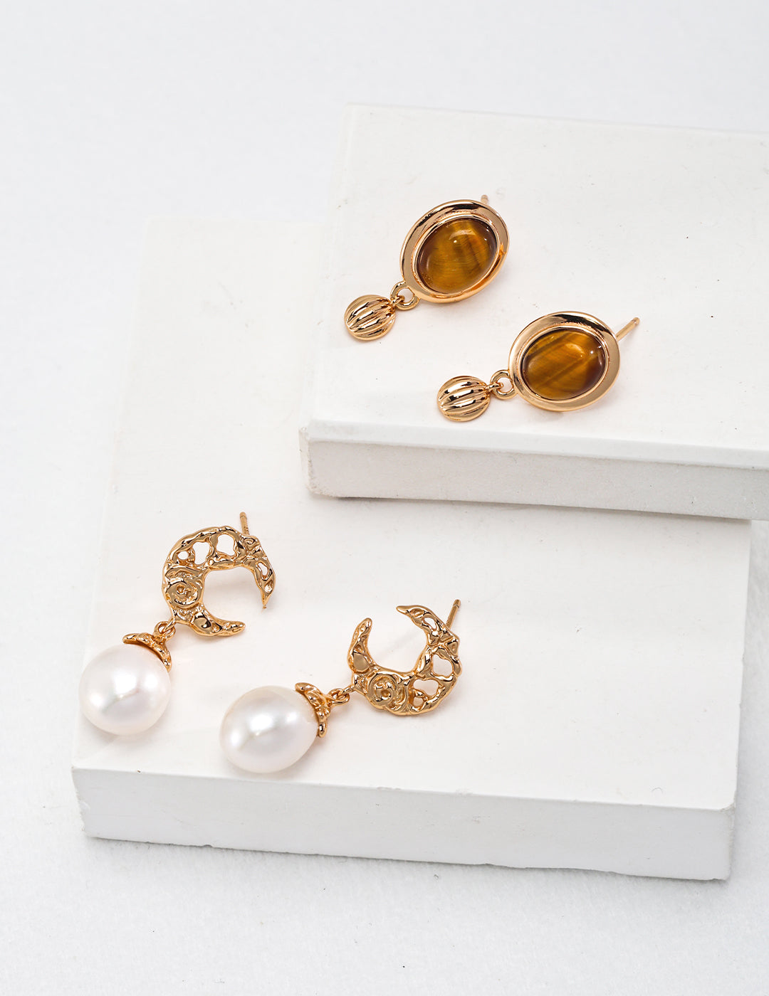 Gold earrings featuring pearl embellishments: crescent moon, freshwater pearl, and tiger's eye stone dangles.