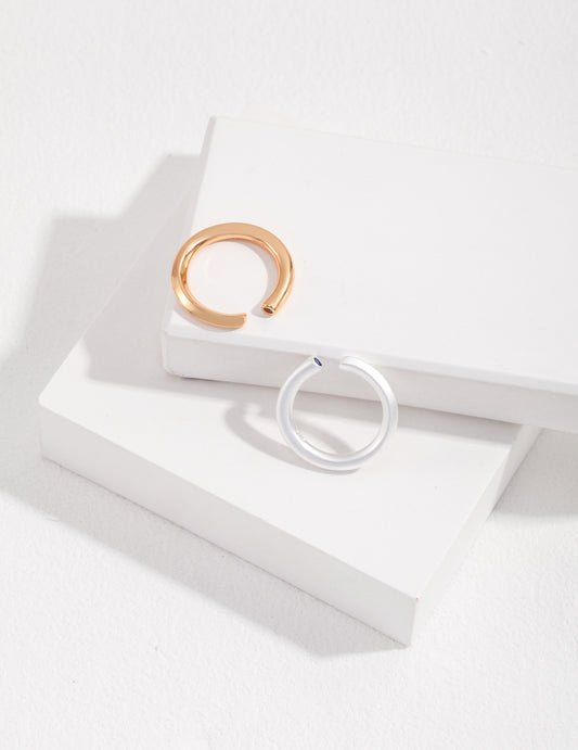 Two minimalist silver and gold rings with aquamarine stones on a white surface.