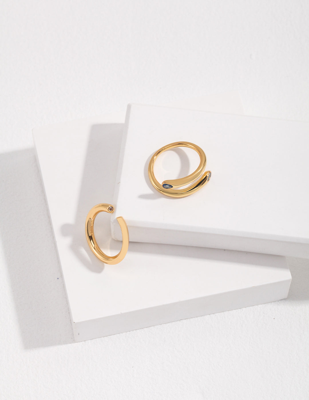 A pair of sleek gold rings with aquamarine stones, showcasing unique designs, placed on a white surface.