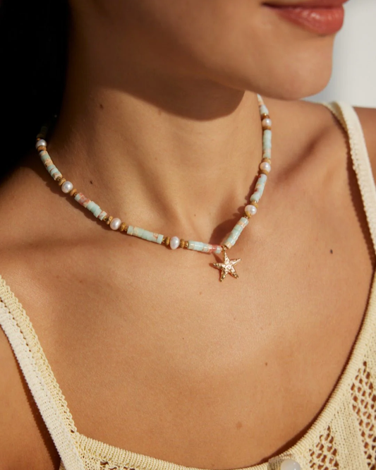 A woman displays a necklace adorned with a starfish and pearls, highlighting a coastal-themed fashion choice.