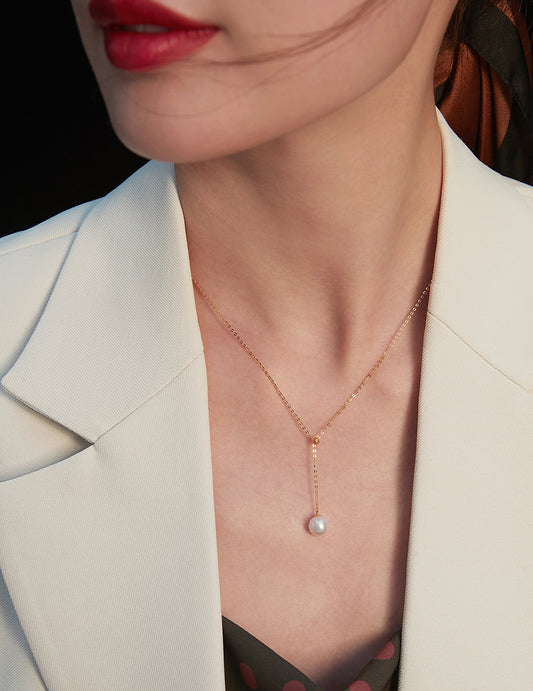 A woman dressed in a white blazer, showcasing a beautiful karat gold necklace with freshwater pearls.